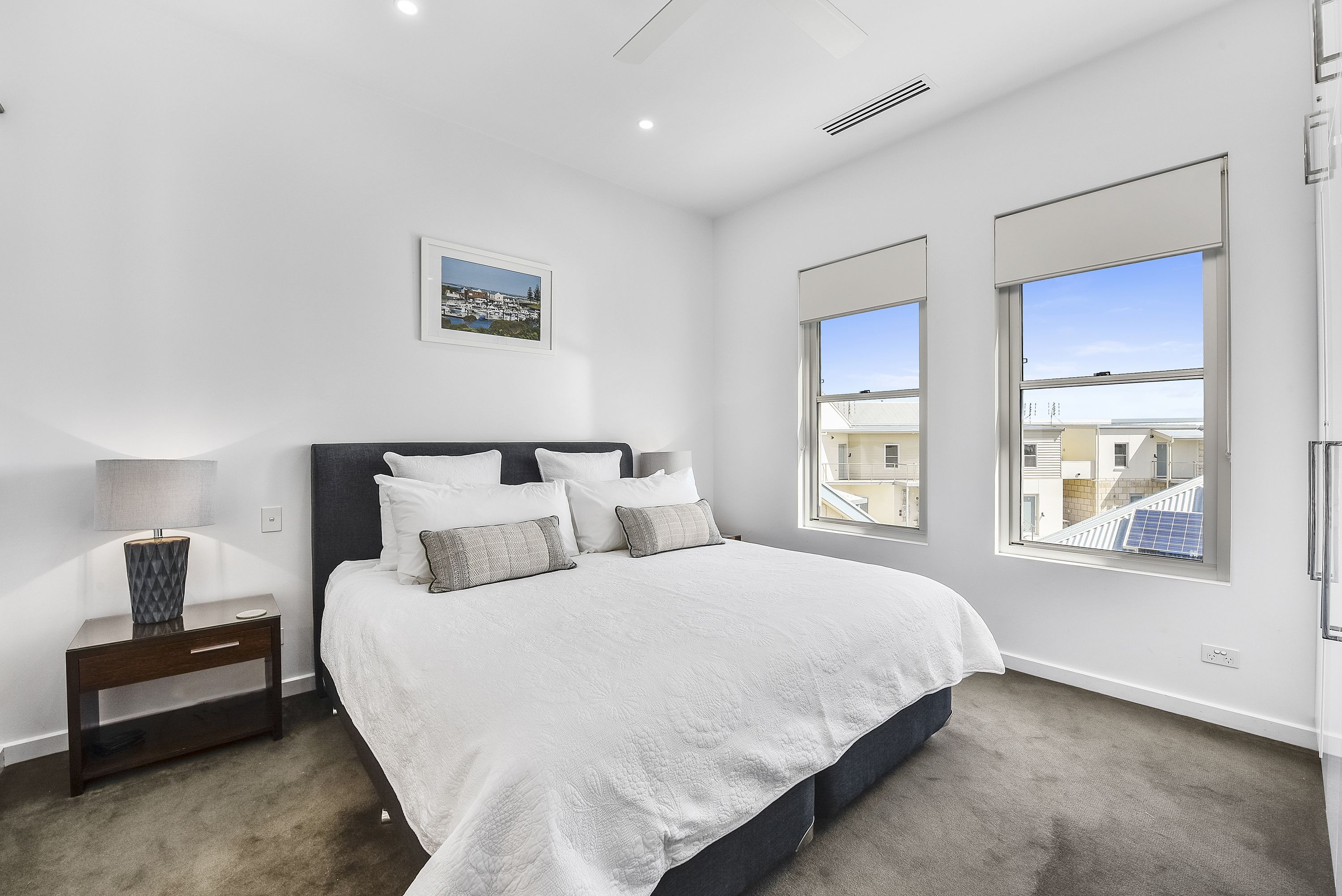 A bedroom with a large bed, a nightstand, a lamp, and a framed picture on the wall.