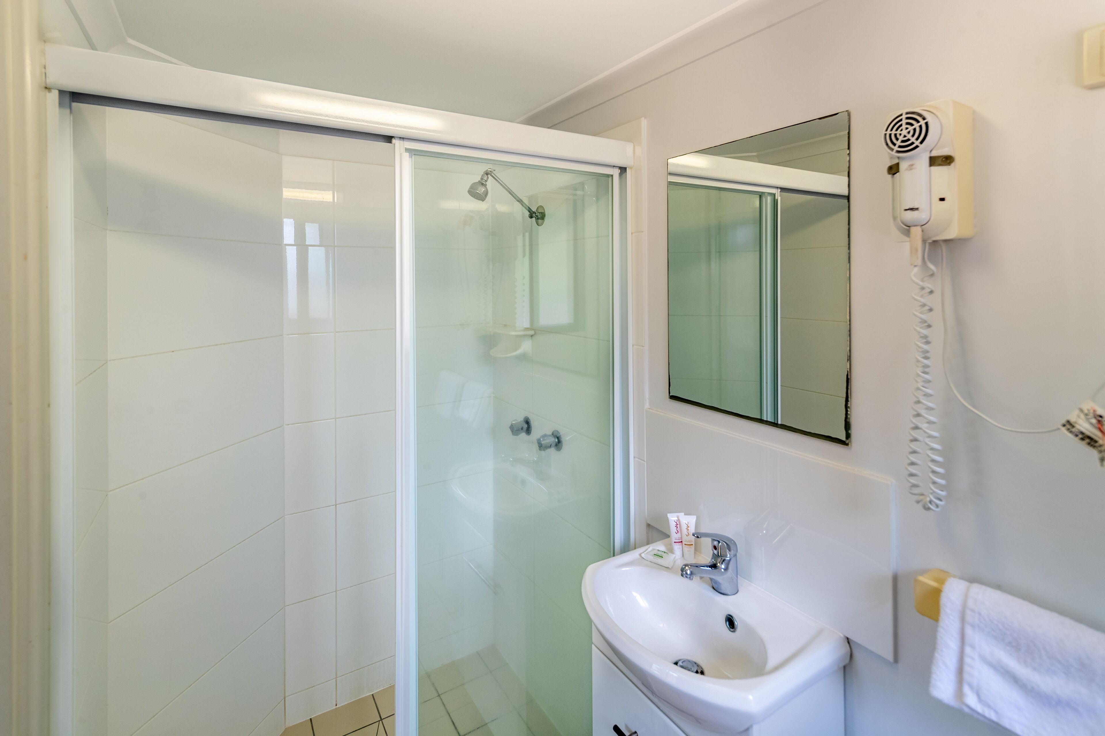 A modern bathroom with a glass-enclosed shower, a white sink with a mirror above it, and a hairdryer mounted on the wall.