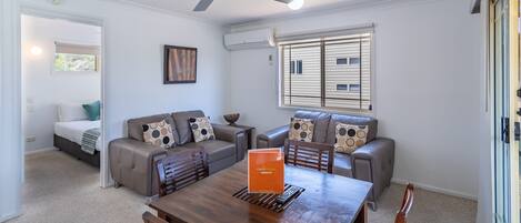 A modern living room with a dining table, sofas, and a ceiling fan.