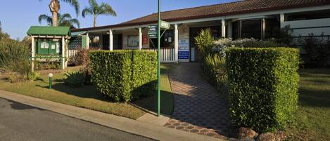 A building with a covered entrance, a sign indicating an office, and a pathway leading to the entrance.