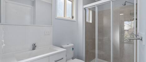 A modern bathroom with a white vanity, a toilet, and a glass-enclosed shower.