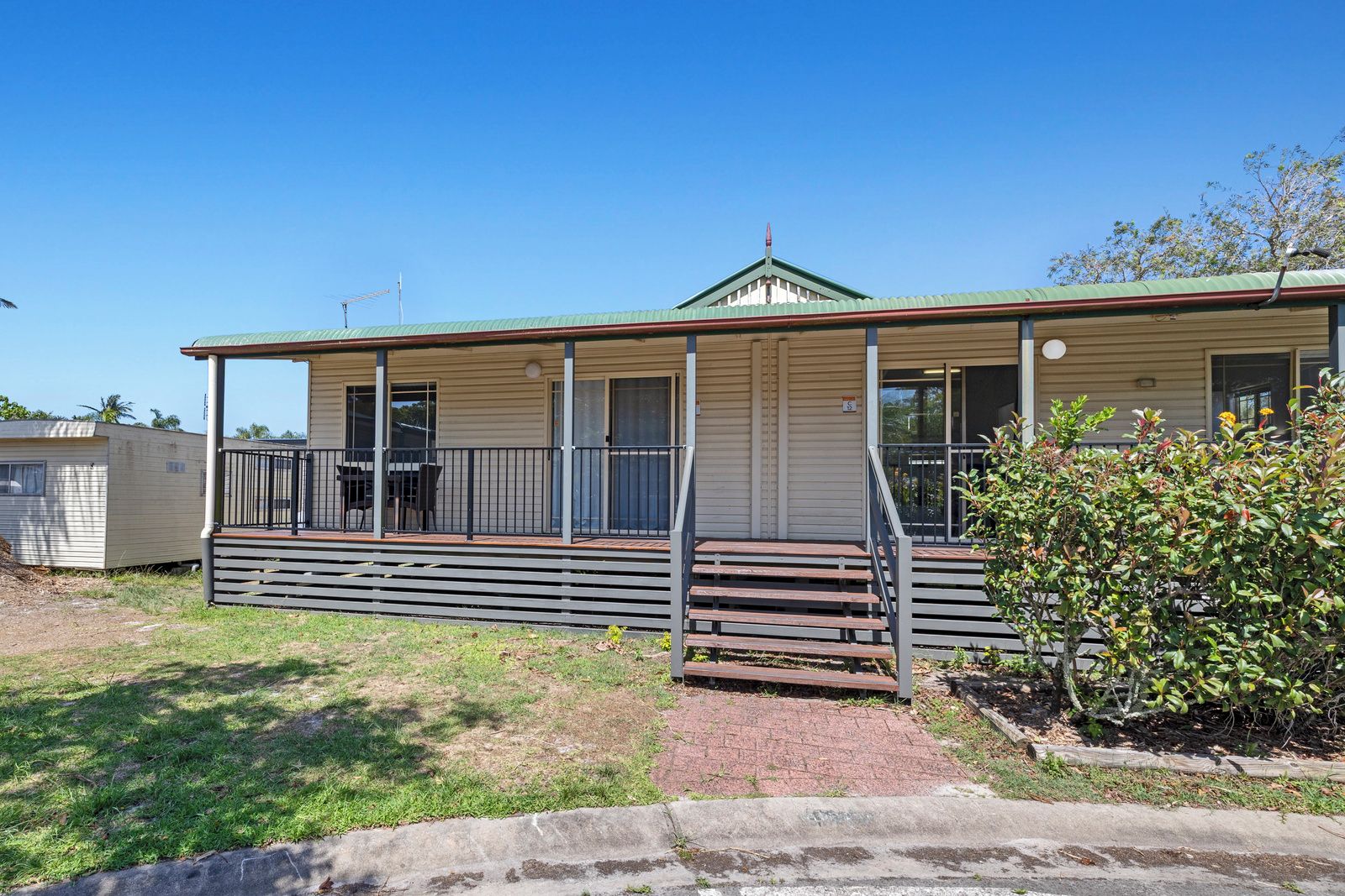 A single-story mobile home with a porch, a small deck, and a fenced yard.