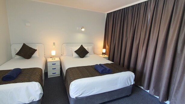 A hotel room with two single beds, each with a pillow and a bedside table with a lamp. - Silver Oaks Motel (Gilgandra)