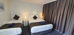 Una habitación de hotel con dos camas individuales, cada una con una almohada y una mesita de noche con lámpara.