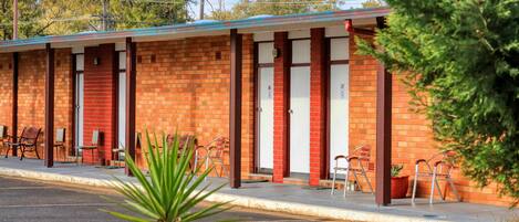 Un motel con paredes de ladrillo, habitaciones numeradas y mobiliario exterior.