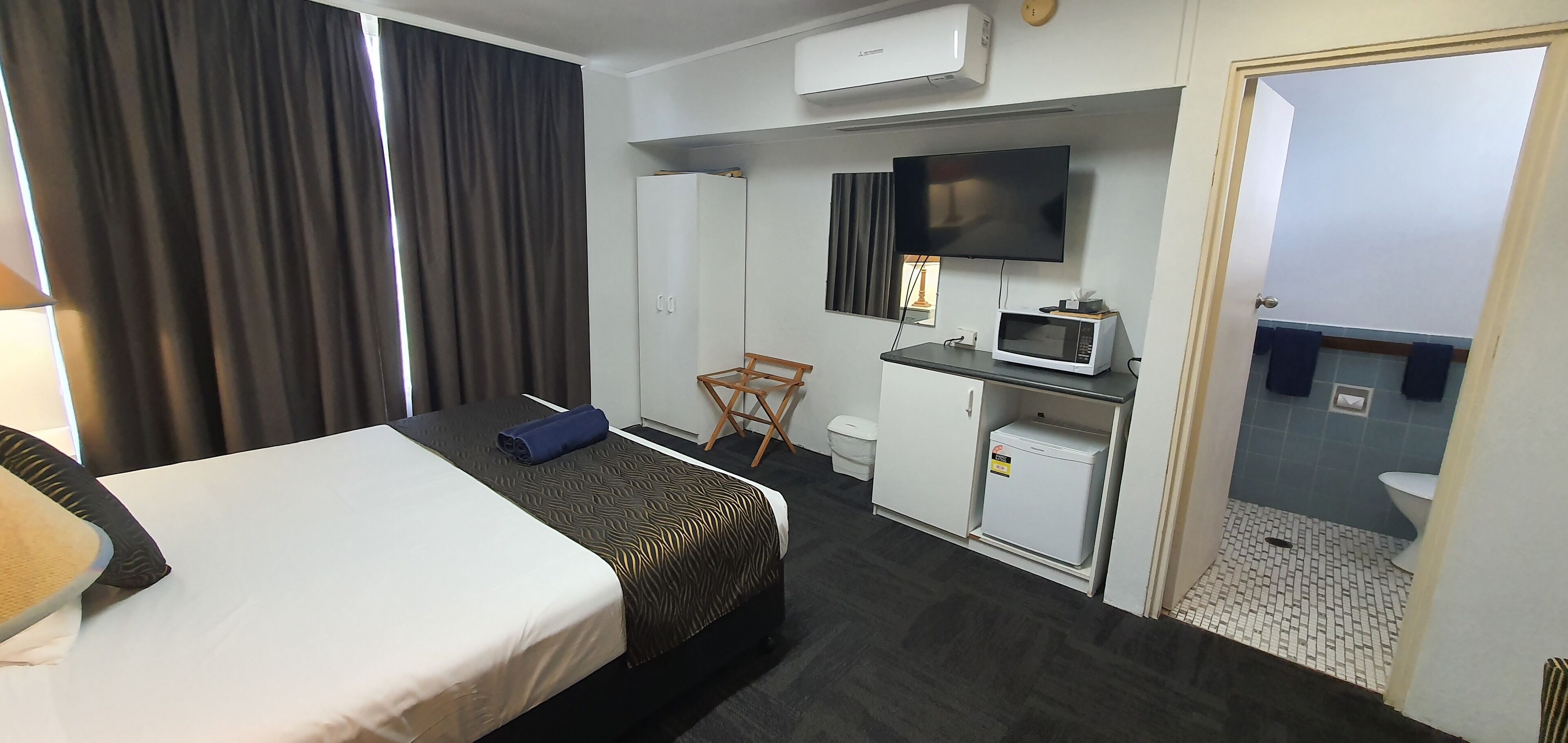 Una habitación de hotel con una cama, un escritorio con televisor, microondas y un refrigerador pequeño.
