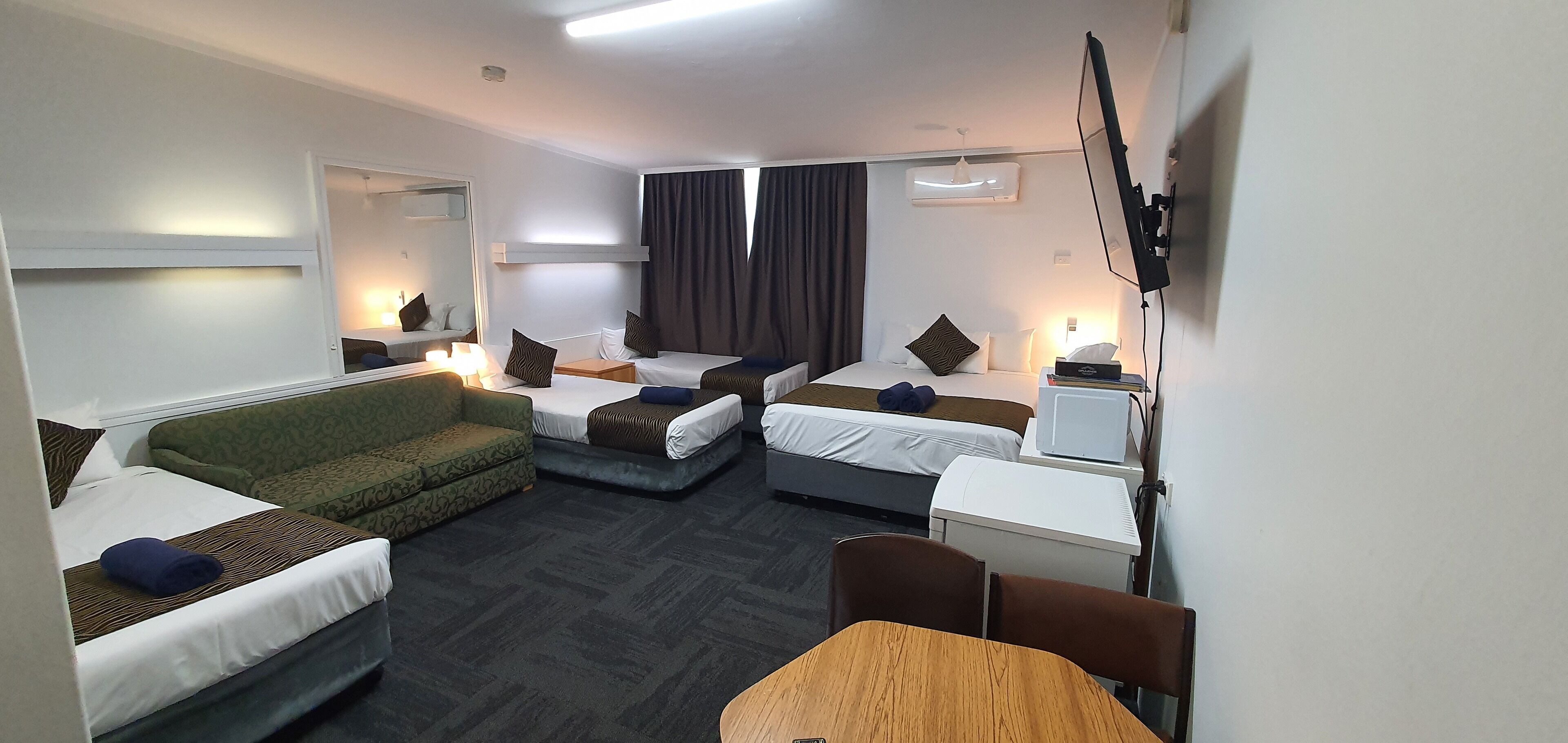 A hotel room with two single beds, a sofa, a small table, and a mirror.