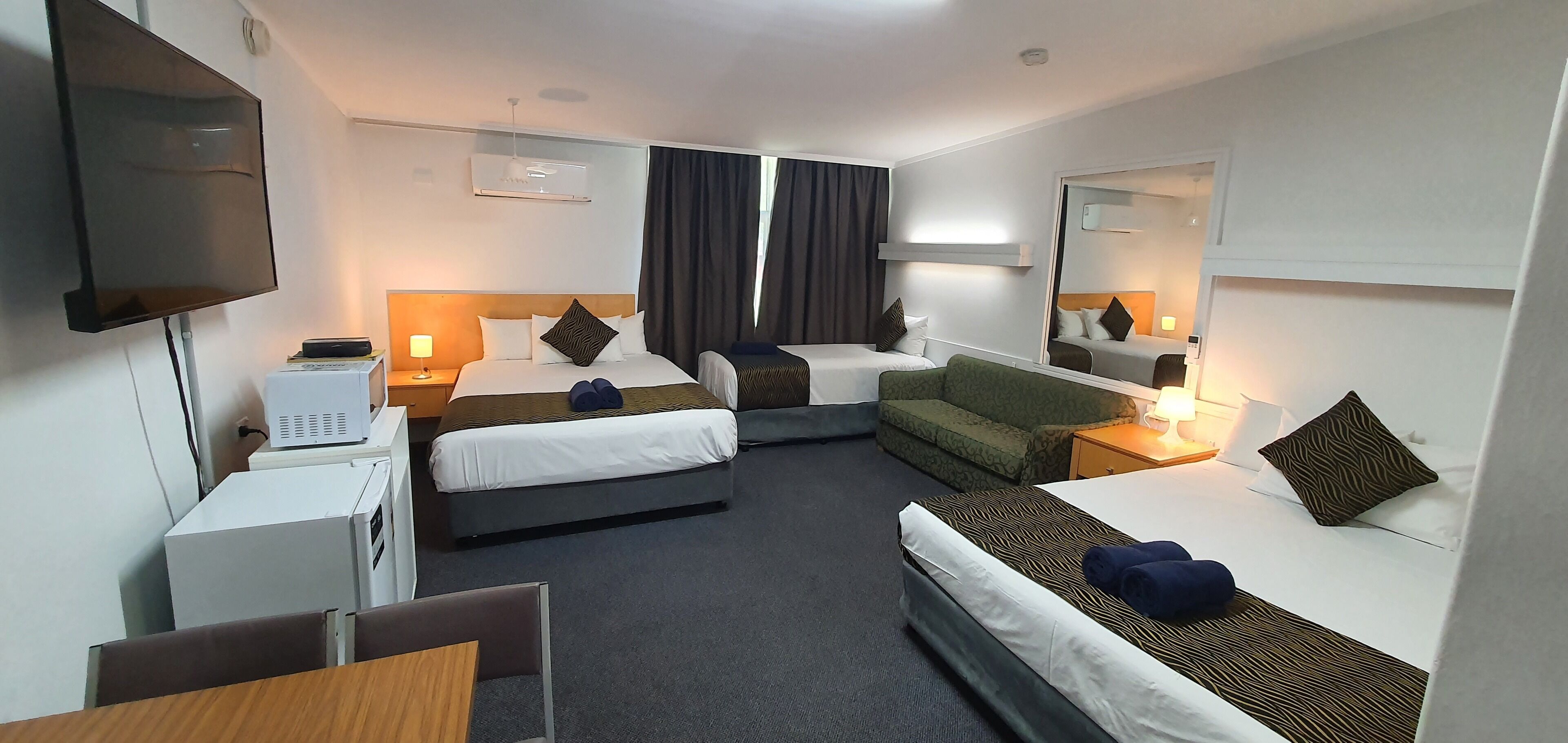 Ein Hotelzimmer mit zwei Einzelbetten, einer Schlafcouch, einem Schreibtisch mit Stuhl, einem Flachbildfernseher und einer Minibar.