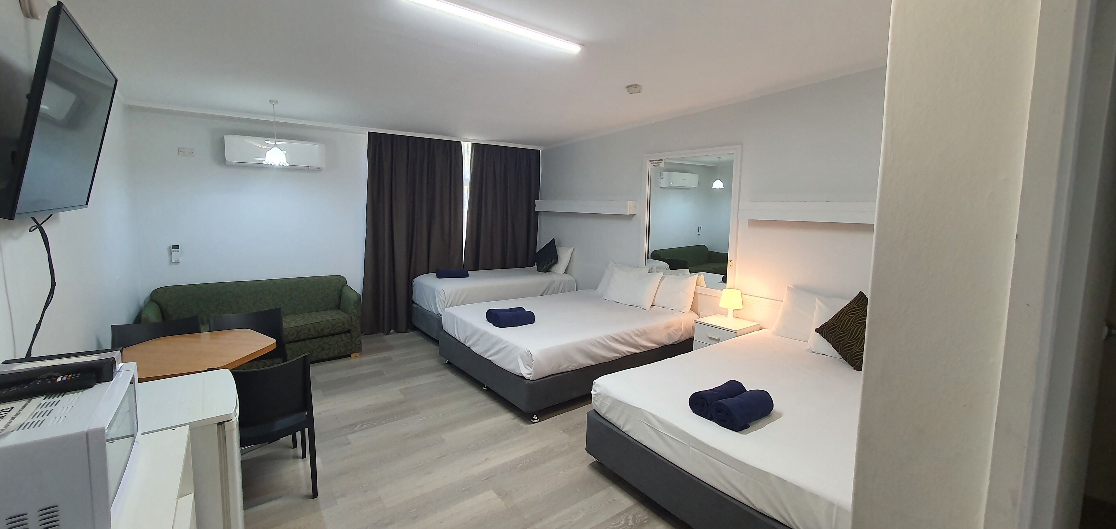 A hotel room with two beds, a desk, a chair, a TV, and an air conditioning unit.