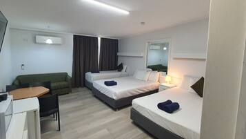 A hotel room with two beds, a desk, a chair, a TV, and an air conditioning unit.