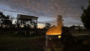 A metal barrel with a visible flame, surrounded by a grassy area and trees. - Silver Oaks Motel (Gilgandra)