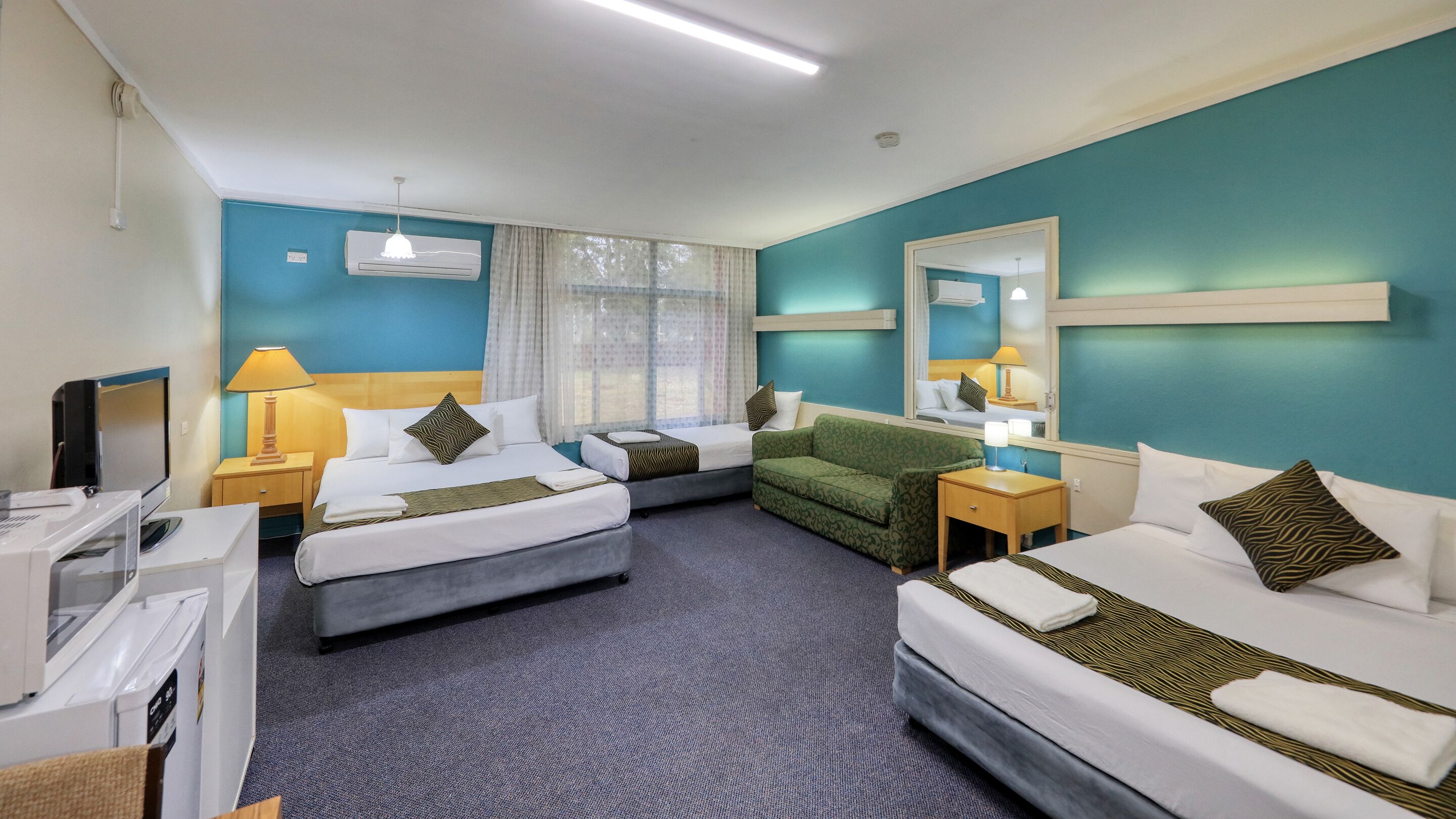 A hotel room with two beds, a sofa, a TV, and a minibar.