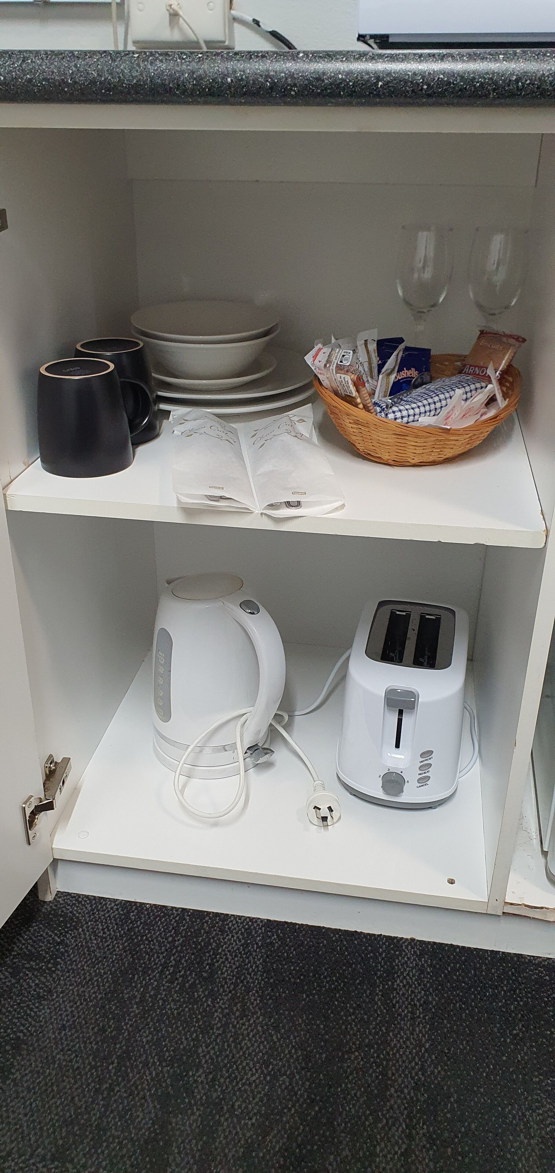 A kitchen with a kettle, toaster, black mugs, and a basket with items.