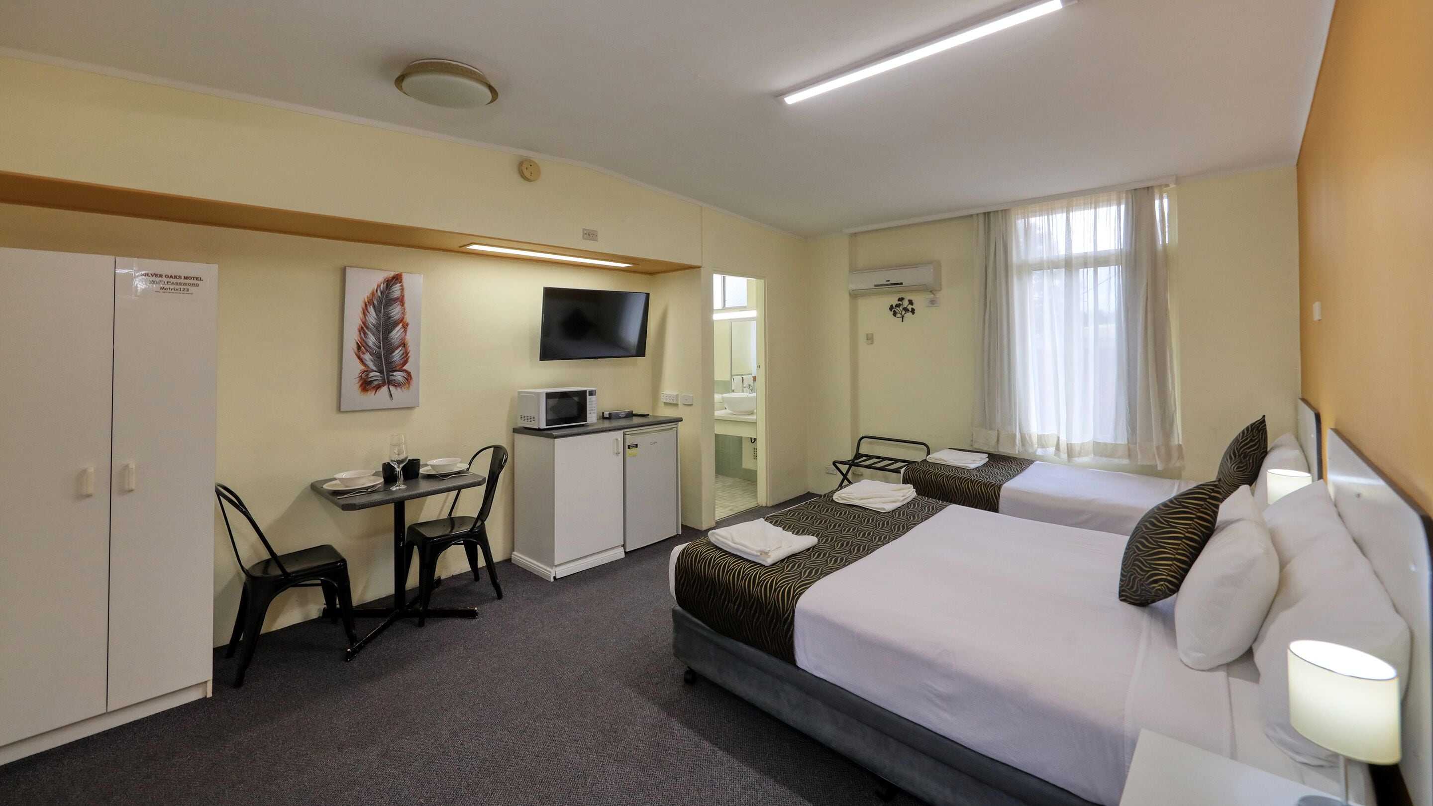 Habitación de hotel con dos camas, un escritorio con silla, televisión y una kitchenette pequeña.