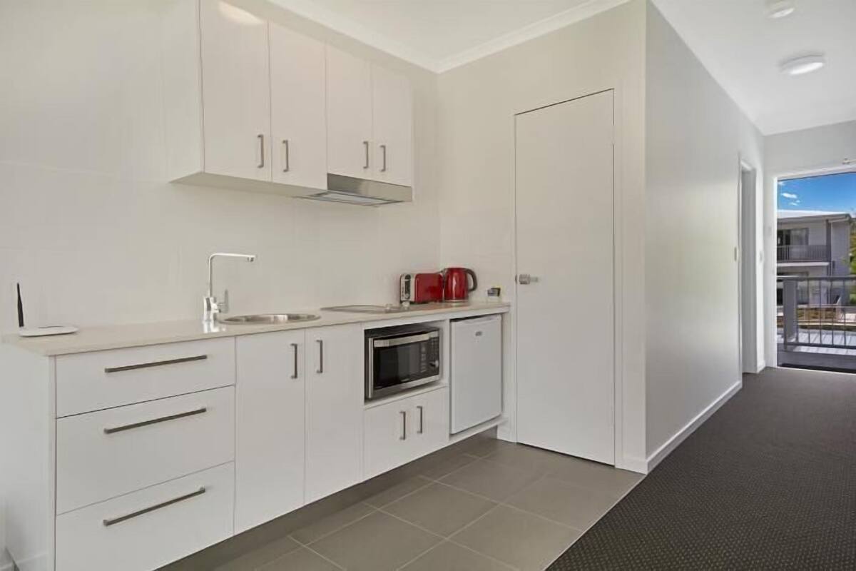 A modern kitchen with white cabinetry, a stainless steel oven, and a red kettle.