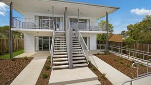 A modern two-story house with a central staircase, a covered balcony, and a fenced backyard. - Cooroy Luxury Motel Apartments Noosa (Cooroy)