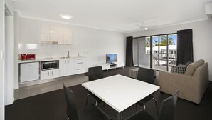 A modern kitchen with white cabinets, a dining area with a white table and chairs, and a sofa. - Cooroy Luxury Motel Apartments Noosa (Cooroy)