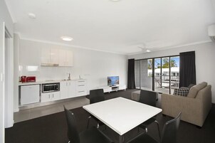A modern kitchen with white cabinets, a dining area with a white table and chairs, and a sofa.