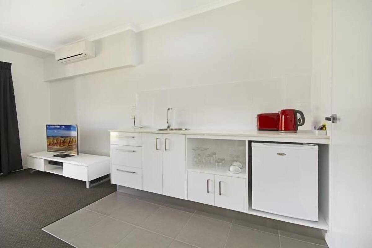 A modern kitchen with white cabinetry, a built-in refrigerator, and a coffee machine.