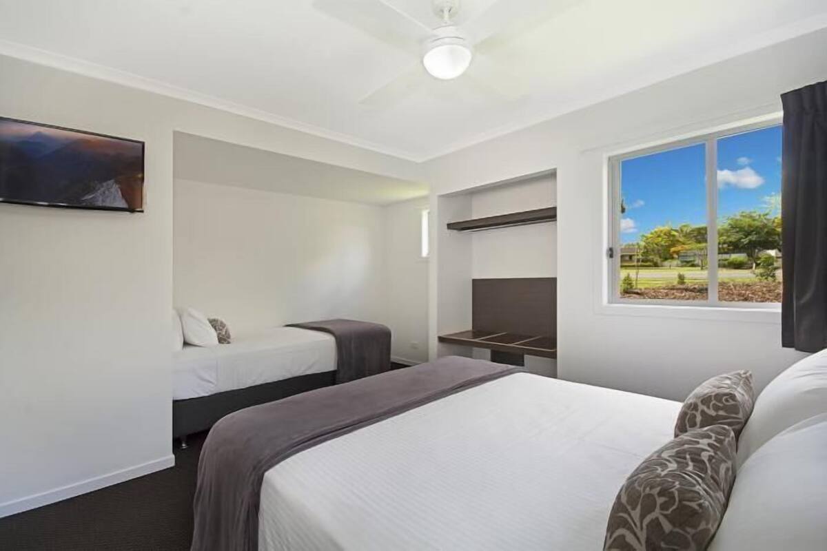 A hotel room with a large bed, a smaller bed, a TV, a desk, and a window with a view of the outdoors.