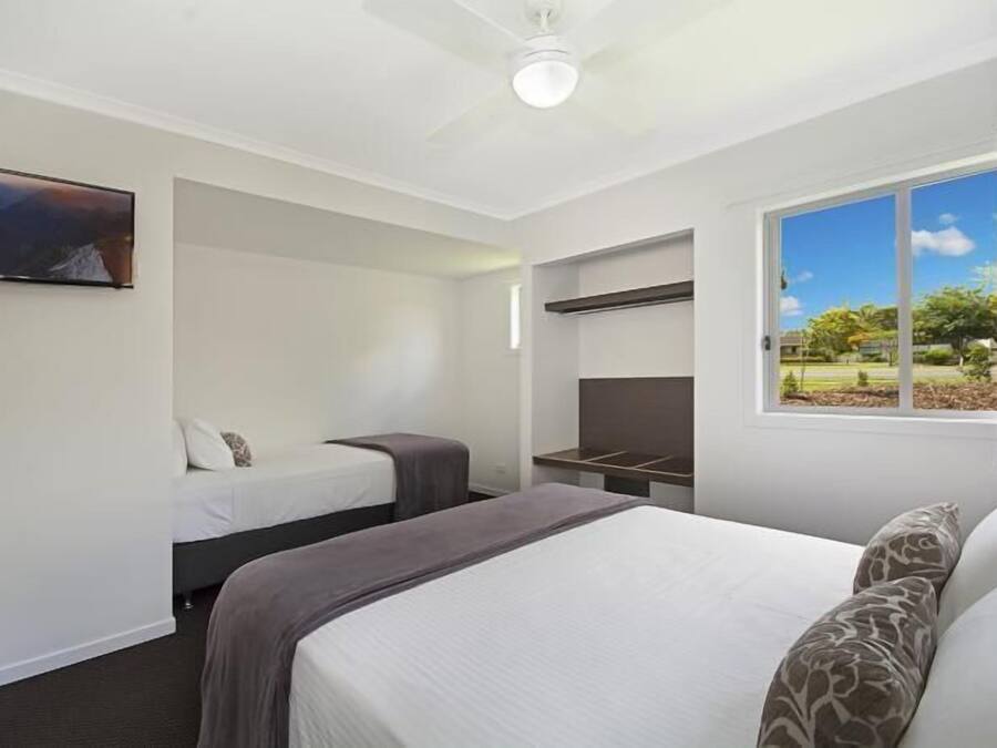 A hotel room with a large bed, a smaller bed, a TV, a desk, and a window with a view of the outdoors.