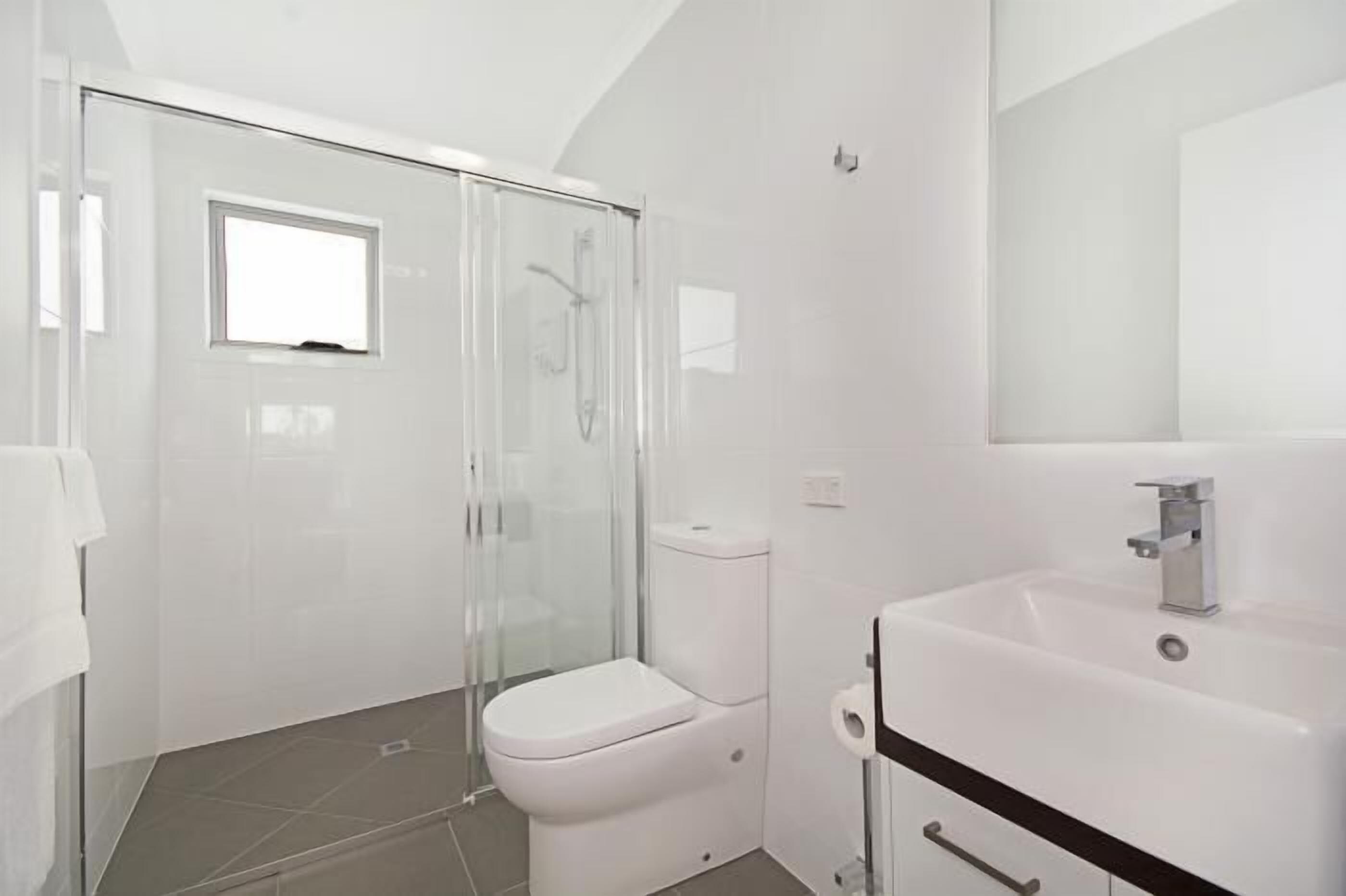 Un bagno moderno con box doccia in vetro, un water bianco e un lavandino con specchio.