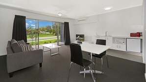A modern living room with a sofa, a dining table, and a TV. There is a kitchen area with cabinets and a refrigerator. - Cooroy Luxury Motel Apartments Noosa (Cooroy)
