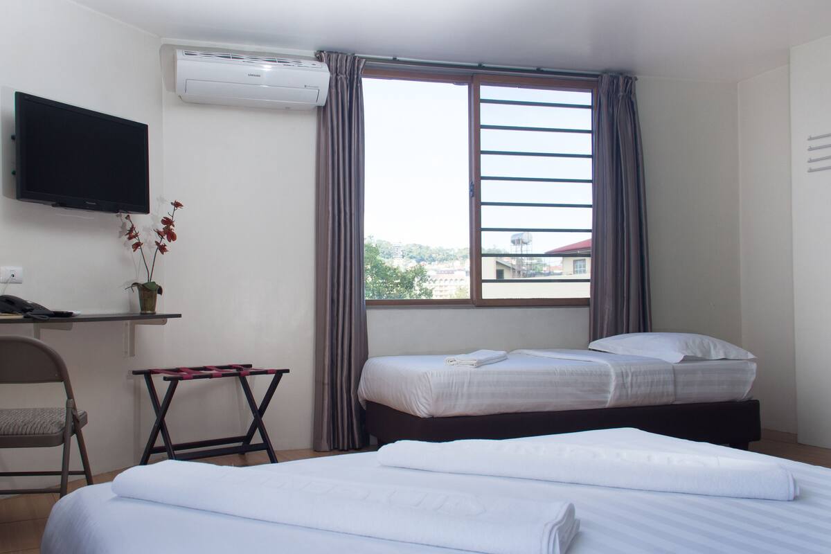 Een hotelkamer met een bed, een bureau met stoel, een aan de muur bevestigde televisie en een raam met gordijnen.