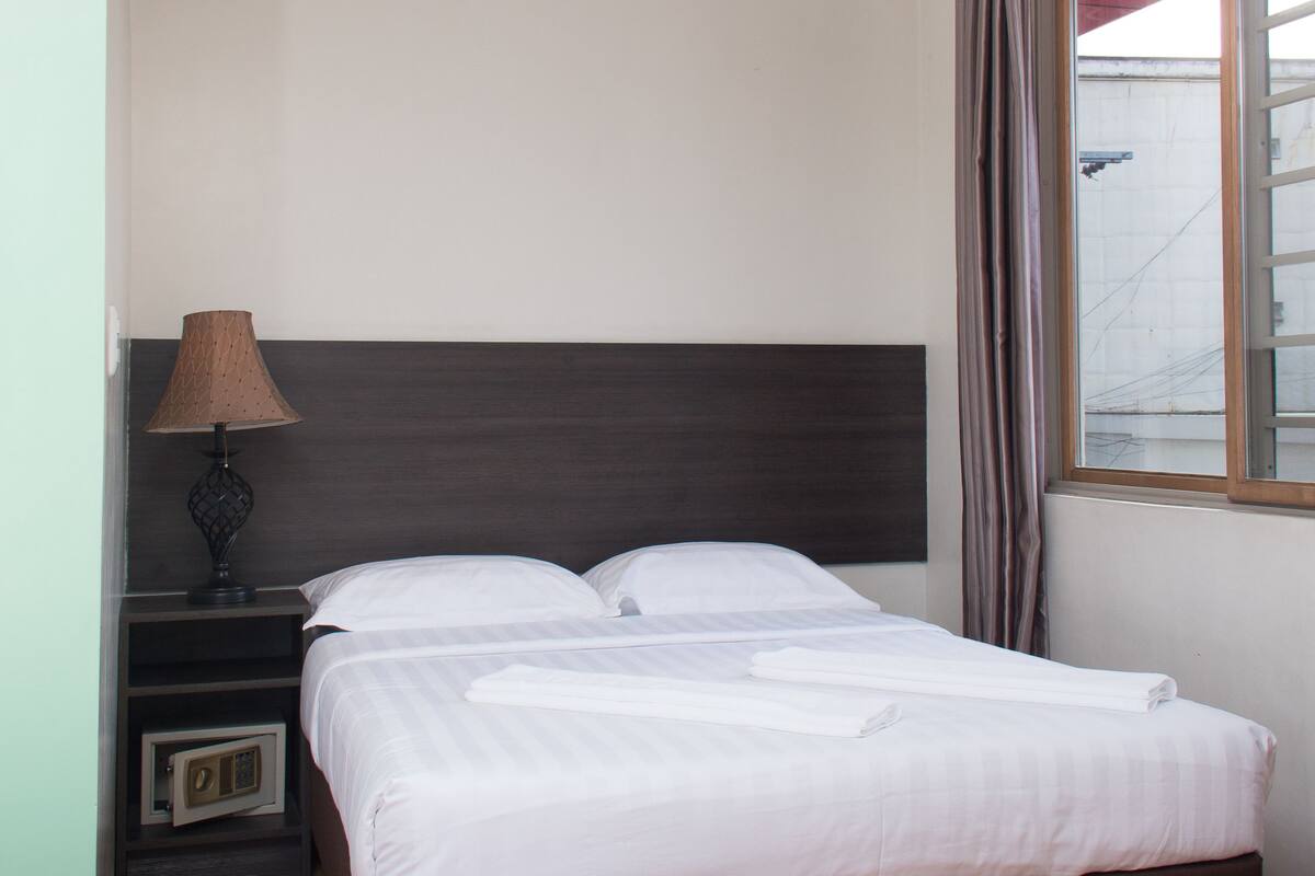 Een netjes opgemaakt bed met witte lakens, een donker hoofdbord en een nachtkastje met een lamp.