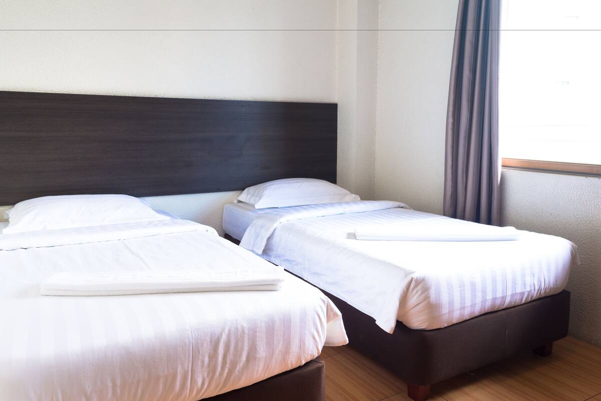 Een hotelkamer met twee eenpersoonsbedden, een donker hoofdeinde en een raam met gordijnen.
