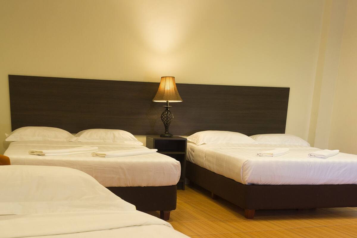Een hotelkamer met drie bedden, een nachtkastje en een lamp.