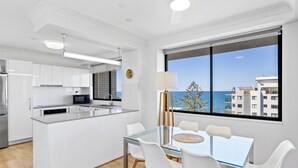 Une cuisine moderne avec des armoires blanches, un four à micro-ondes encastré et un grand îlot central doté d’une table et de chaises en verre.