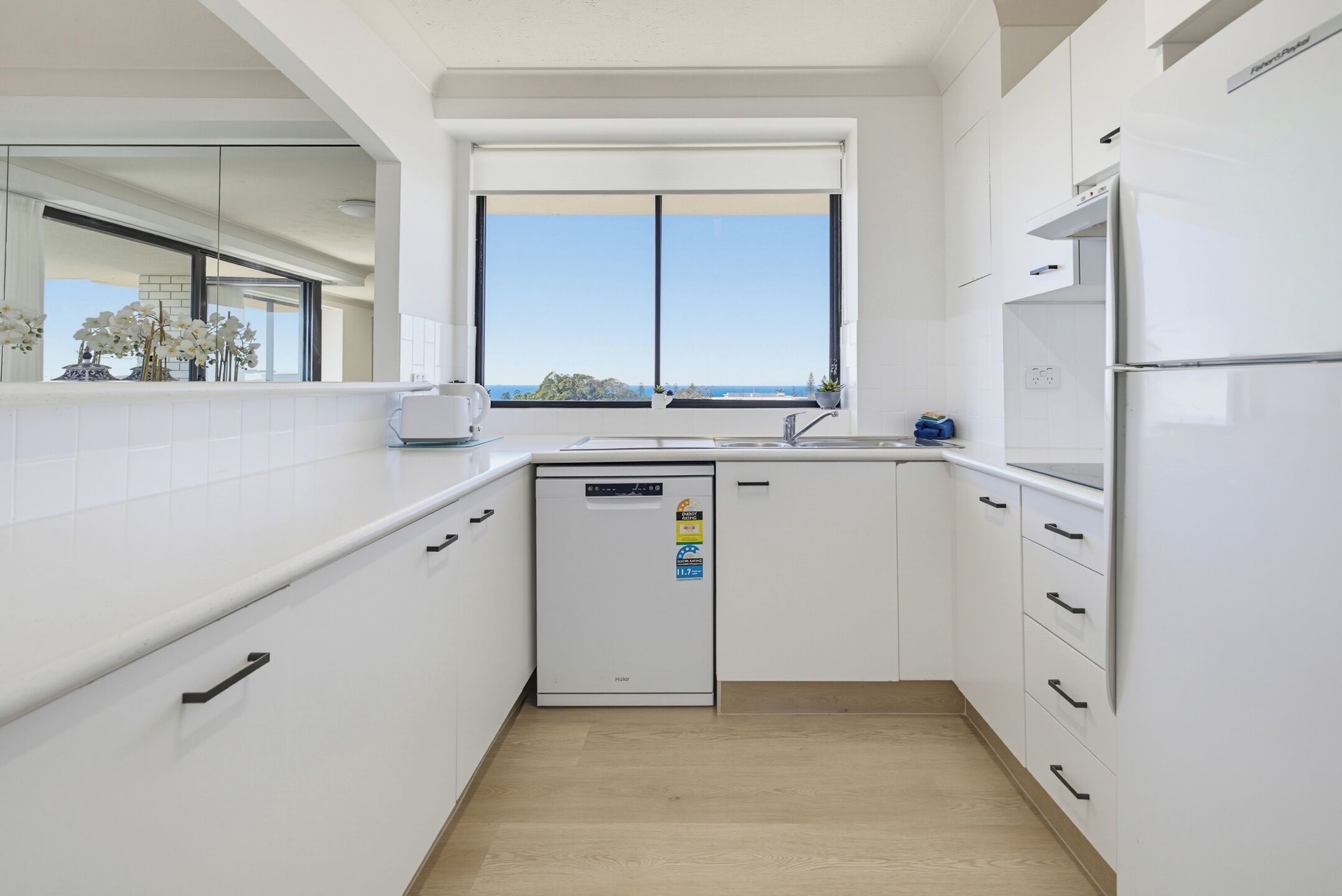 A modern kitchen with white cabinetry, a built-in dishwasher, and a window with a view.