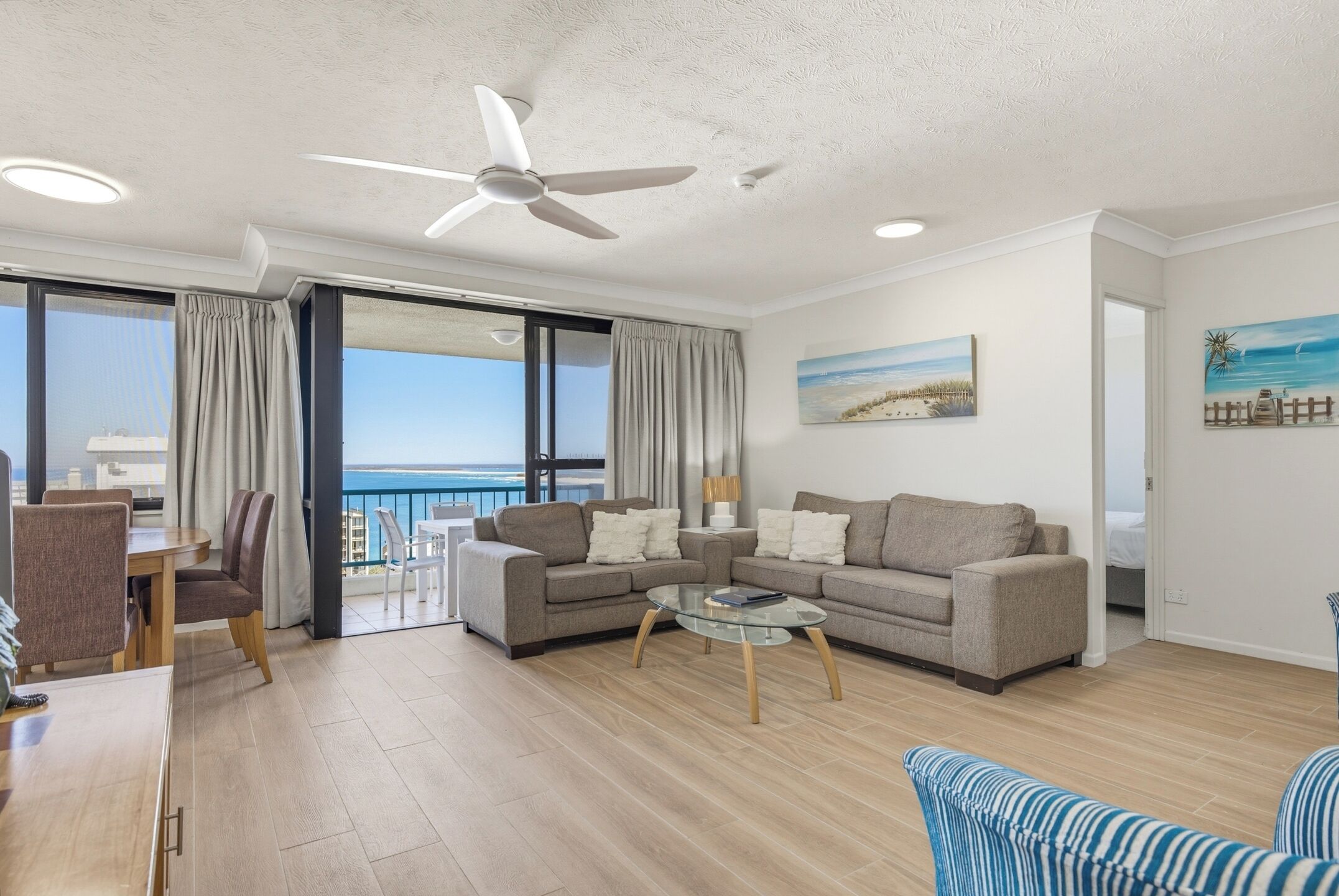 A modern living room with a sofa, armchairs, a glass coffee table, and a ceiling fan.