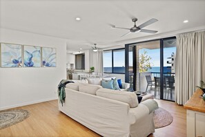 A modern living room with a sofa, a dining area, and a view of the sea. - Burgess @ Kings Beach Apartments (Kings Beach)
