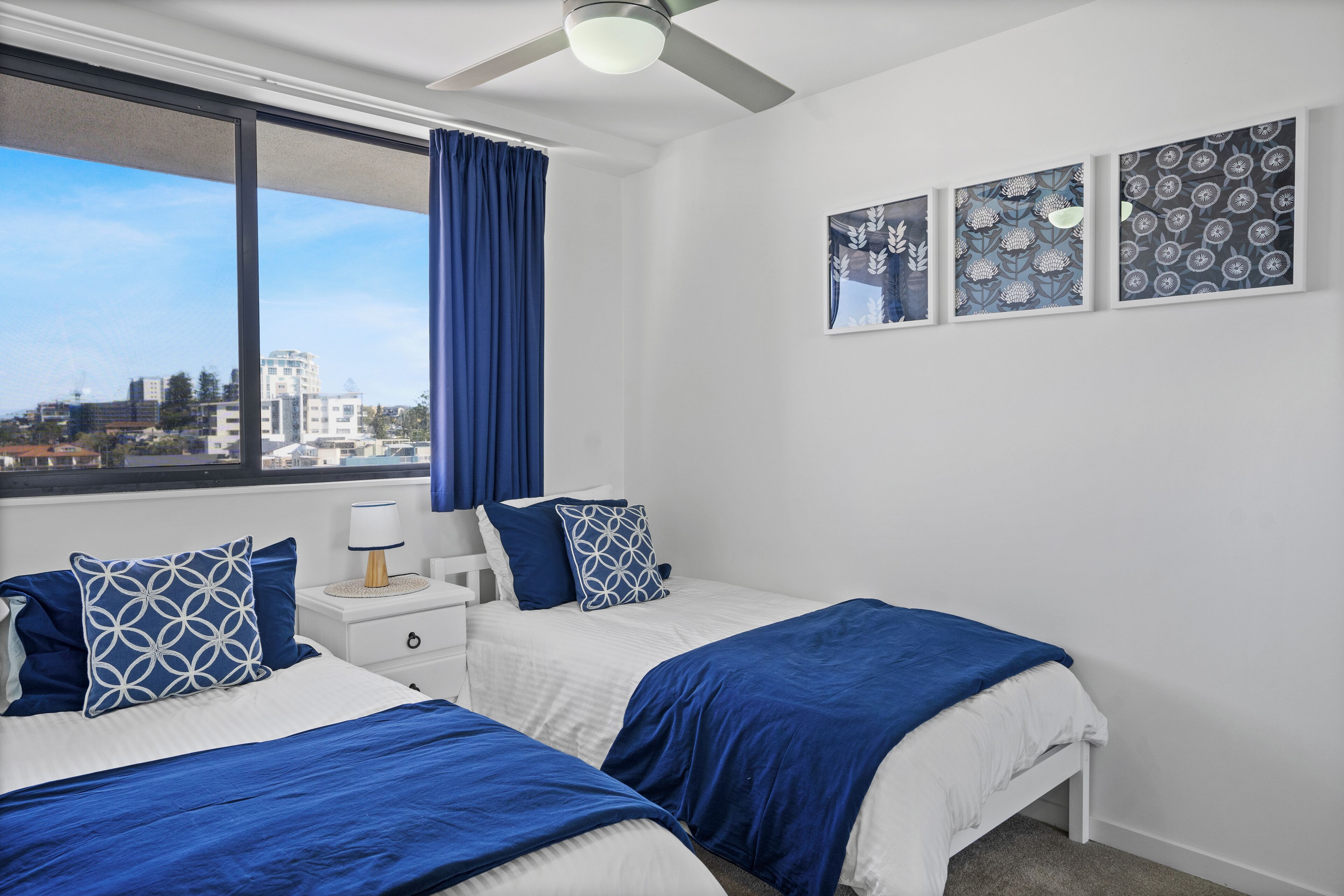 A bedroom with two beds, a nightstand, a ceiling fan, and a window with curtains.