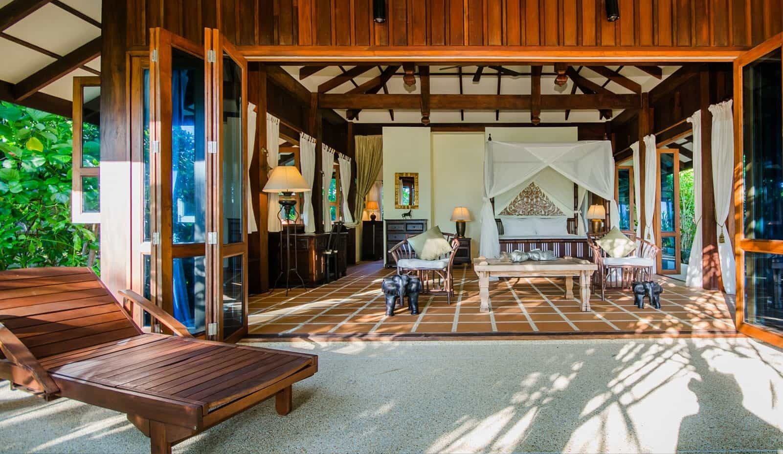 A spacious veranda with wooden flooring, a dining area with chairs, and a view of lush greenery.