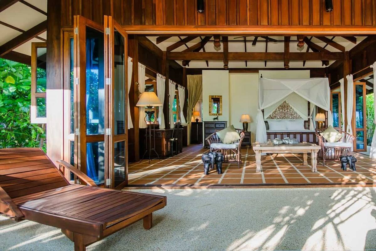 Une véranda spacieuse avec un plancher en bois, un coin repas avec des chaises et une vue sur une végétation luxuriante.
