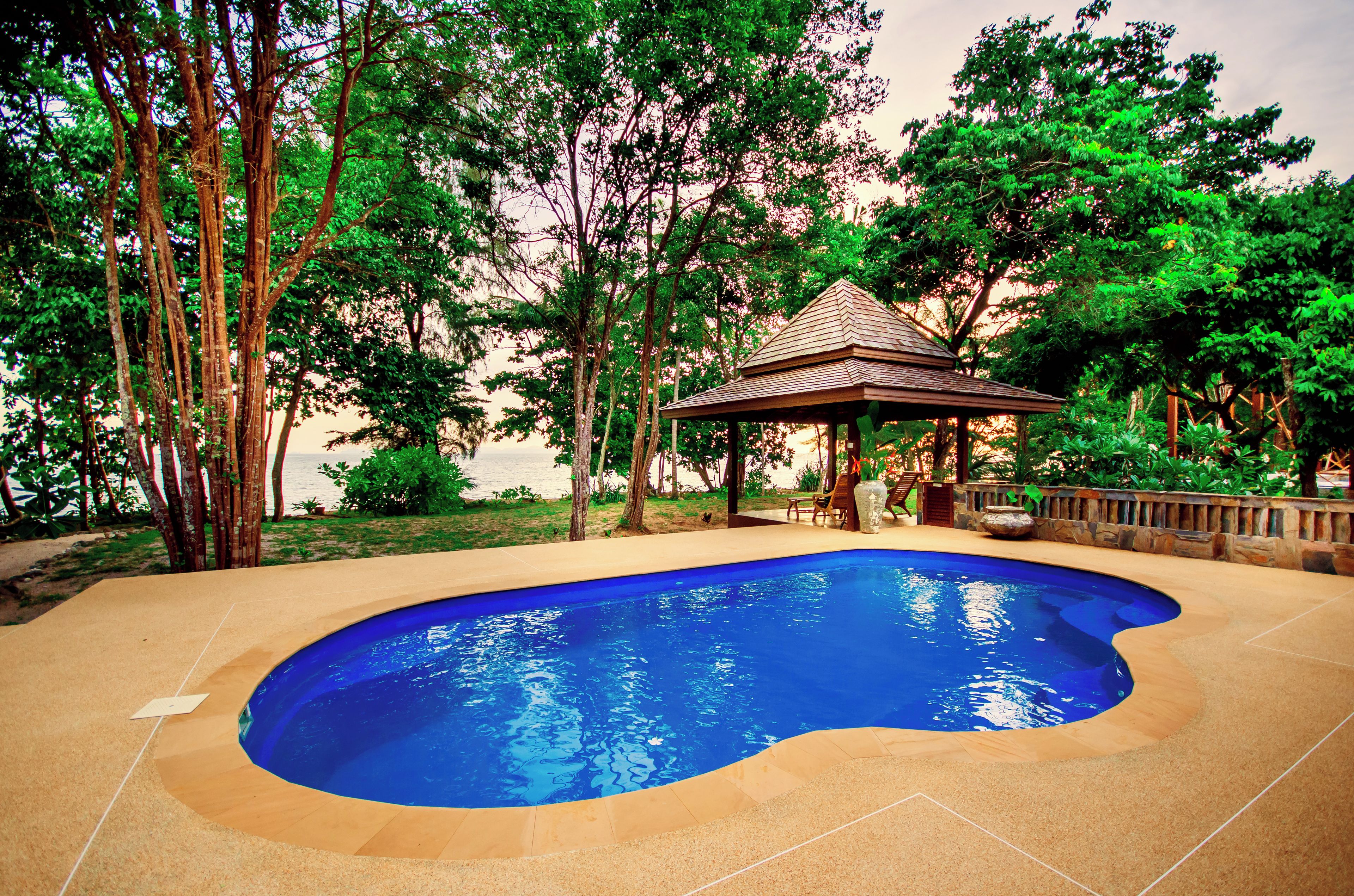 Una piscina con un pabellón, rodeada de árboles y vista al mar.