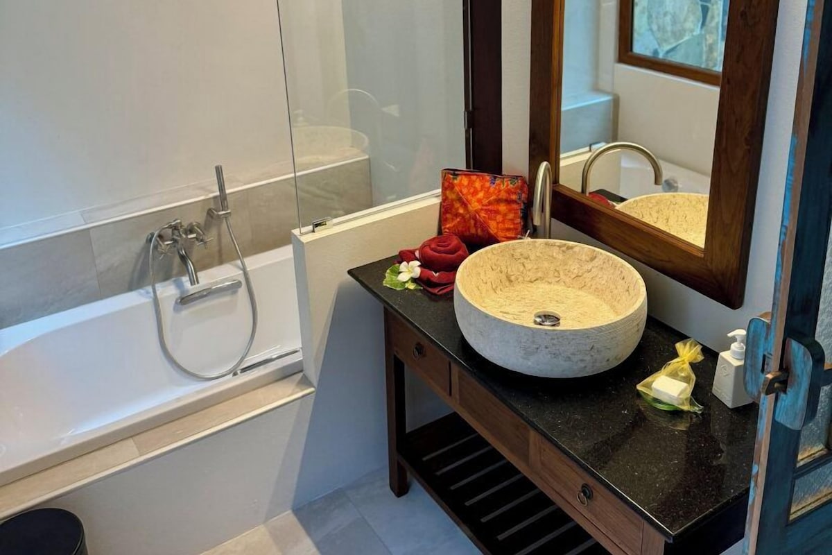 Une salle de bain moderne avec une baignoire sur pieds, un lavabo rond en pierre et un grand miroir avec un cadre en bois.