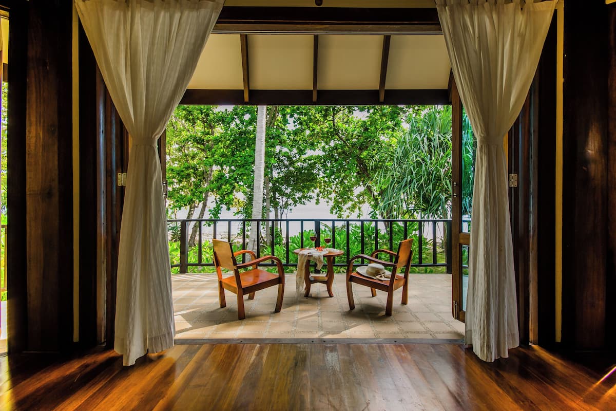 Un espace extérieur abrité avec des chaises et une table en bois, une vue sur la verdure à travers une rambarde et un plancher en bois.