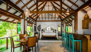 A bedroom with a canopy bed, a dining area with a table and chairs, and a kitchen area with bar stools. - Koh Jum Beach Villas (Nuea Khlong)