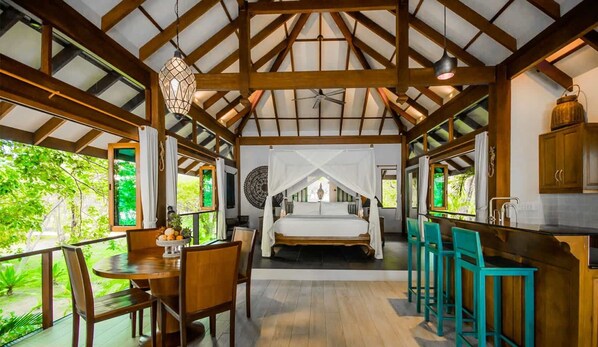 A bedroom with a canopy bed, a dining area with a table and chairs, and a kitchen area with bar stools.