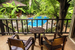 Un balcon donnant sur une piscine, entouré de plantes tropicales et agrémenté d’une table en bois avec des chaises.