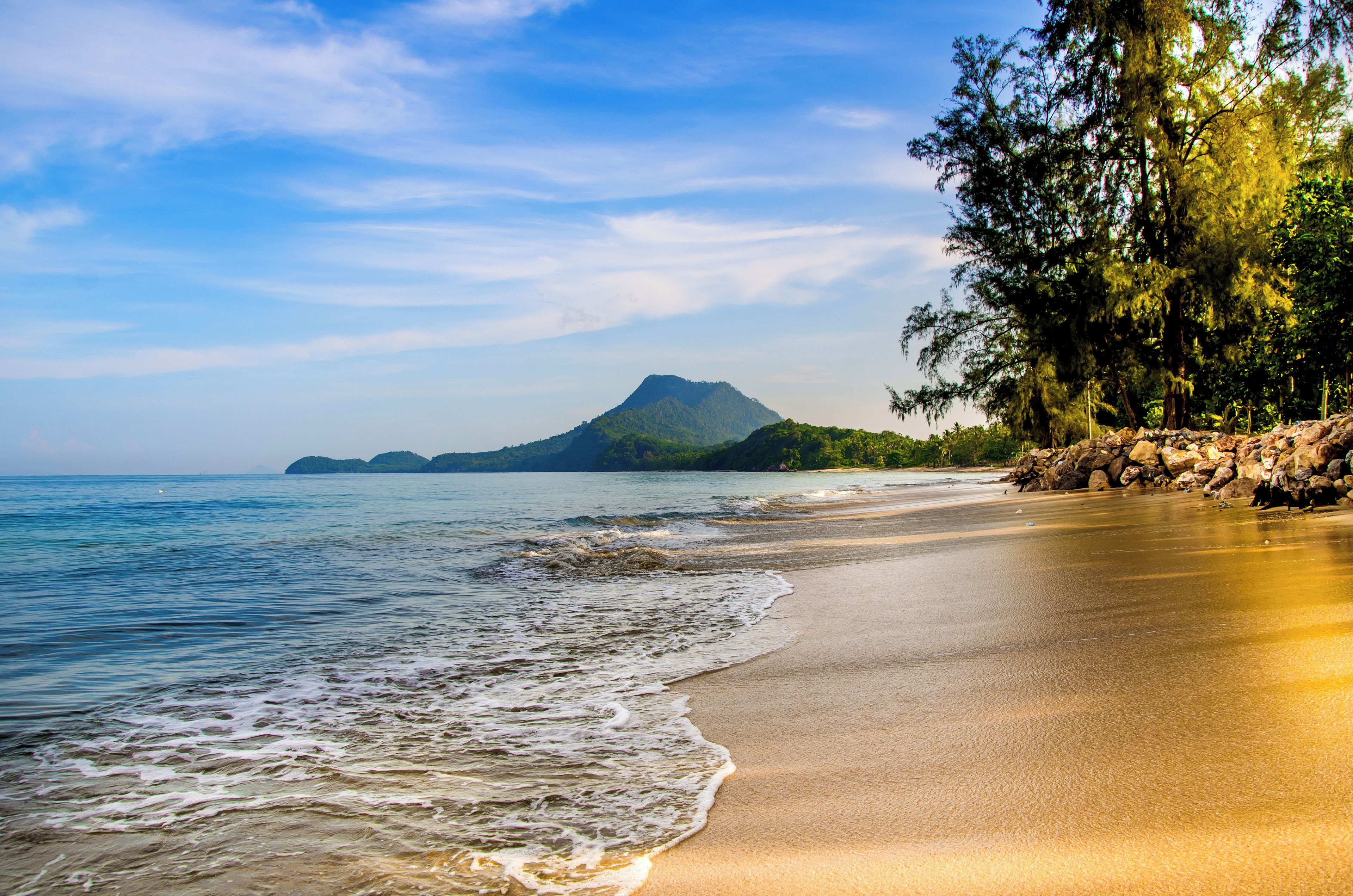 A beach with clear water, a sandy shore, and a mountain in the background.