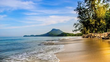 A beach with clear water, a sandy shore, and a mountain in the background.