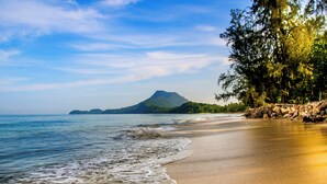 Une plage à l’eau claire, un rivage sablonneux et une montagne en arrière-plan.