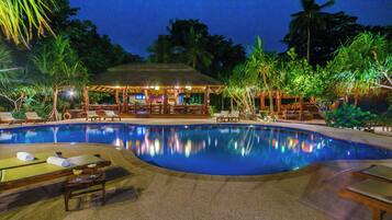 A swimming pool with lounge chairs and a covered seating area.