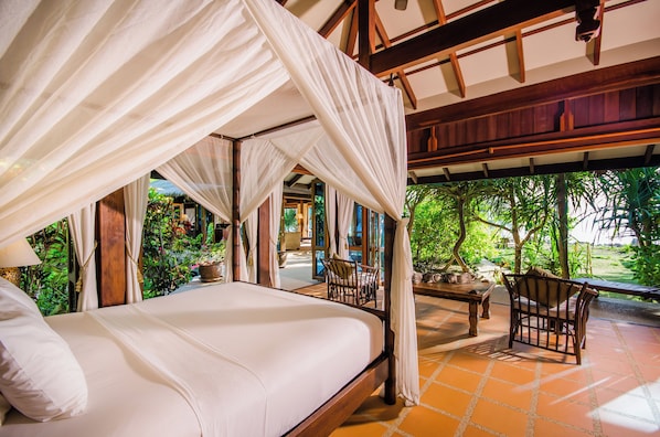 A four-poster canopy bed with a view of a lush garden.