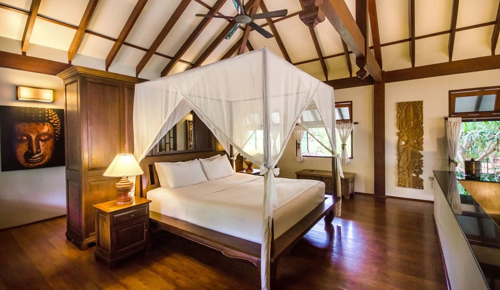 A four-poster bed with a canopy, wooden flooring, a nightstand with a lamp, and a wall-mounted TV.